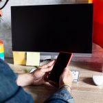 Mężczyzna w biurze z telefonem komórkowym i akcesoriami LGBT oraz gejowską flagą Kultura LGBTQIA