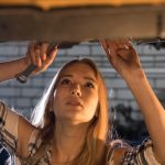 Serwis samochodowy młoda seksowna kobieta mechanik stojąca pod samochodem i patrząc w górę