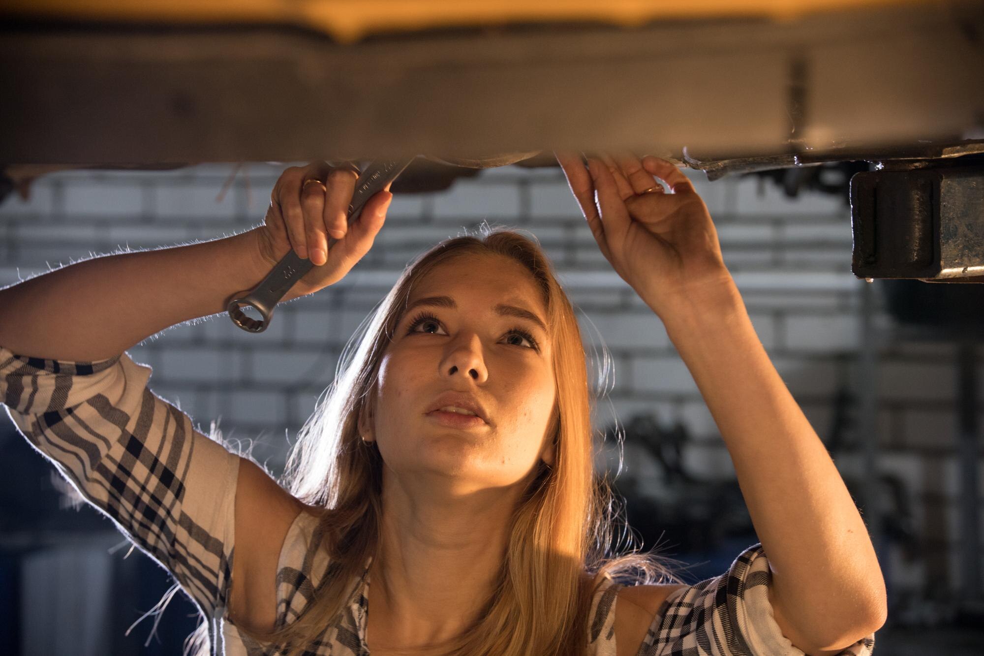 Serwis samochodowy młoda seksowna kobieta mechanik stojąca pod samochodem i patrząc w górę