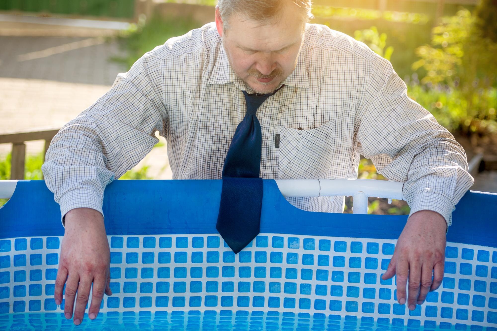 Przystojny mężczyzna w garniturze cierpi z powodu upału przy basenie