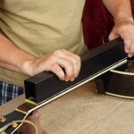 Naprawa i serwis gitar Pracownik szlifuje czarne progi gryfu gitary
