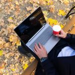 Młody mężczyzna z kawą i korzystaniem z laptopa w jesiennym widoku z góry w parku