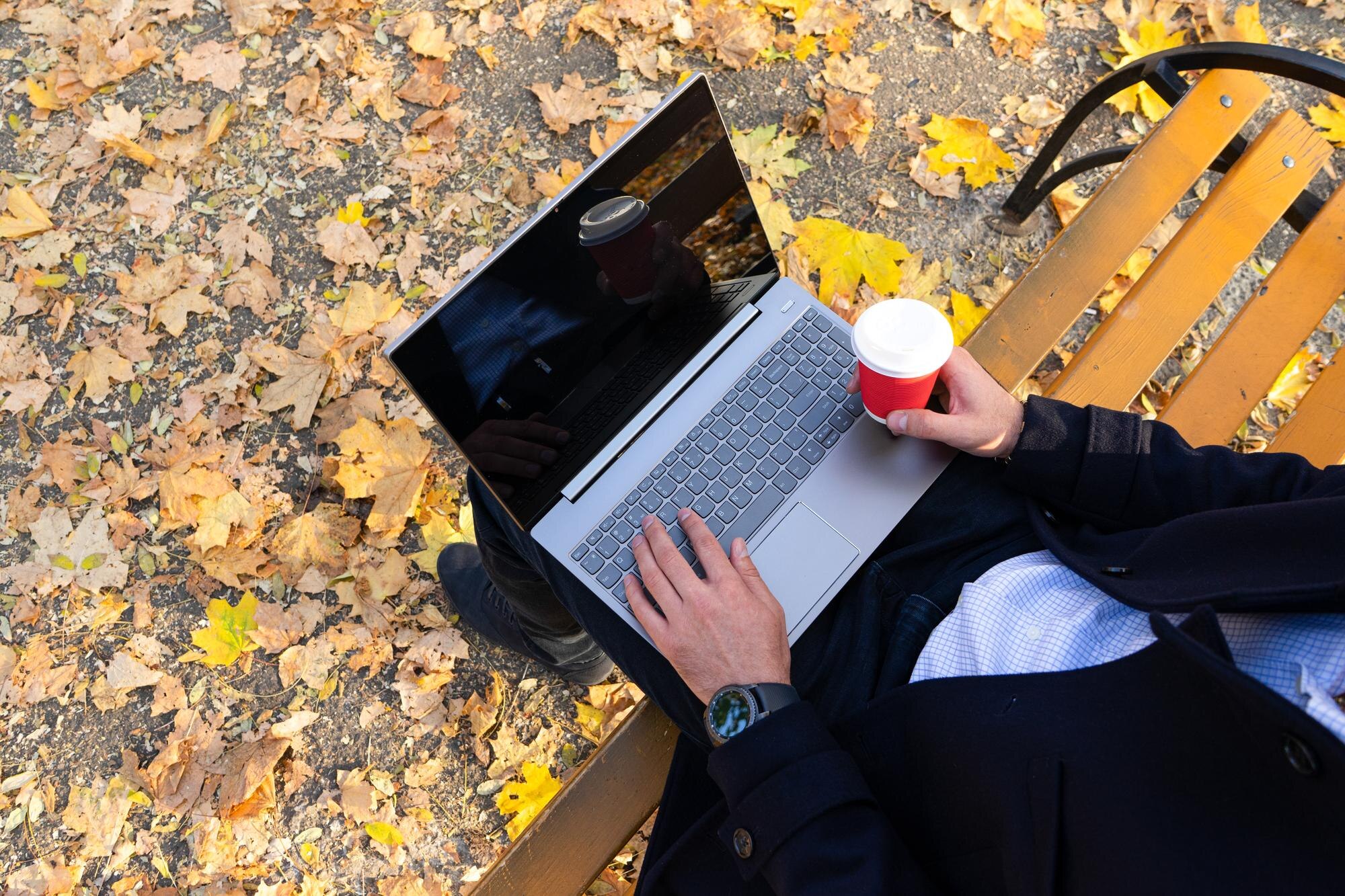 Młody mężczyzna z kawą i korzystaniem z laptopa w jesiennym widoku z góry w parku