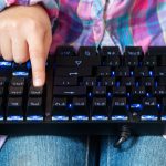 dziecko trzyma na kolanach czarną klawiaturę i palcem wskazującym wciska klawisz Delete