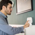 Widok profilu młodego Latynosa używającego klawiatury do uzbrajania domowego systemu alarmowego przed wyjściem