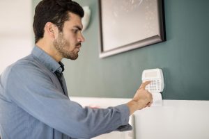 Widok profilu młodego Latynosa używającego klawiatury do uzbrajania domowego systemu alarmowego przed wyjściem