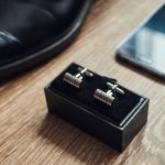 Na stole znajdują się różne akcesoria męskie, takie jak spinki do mankietów na buty i telefon