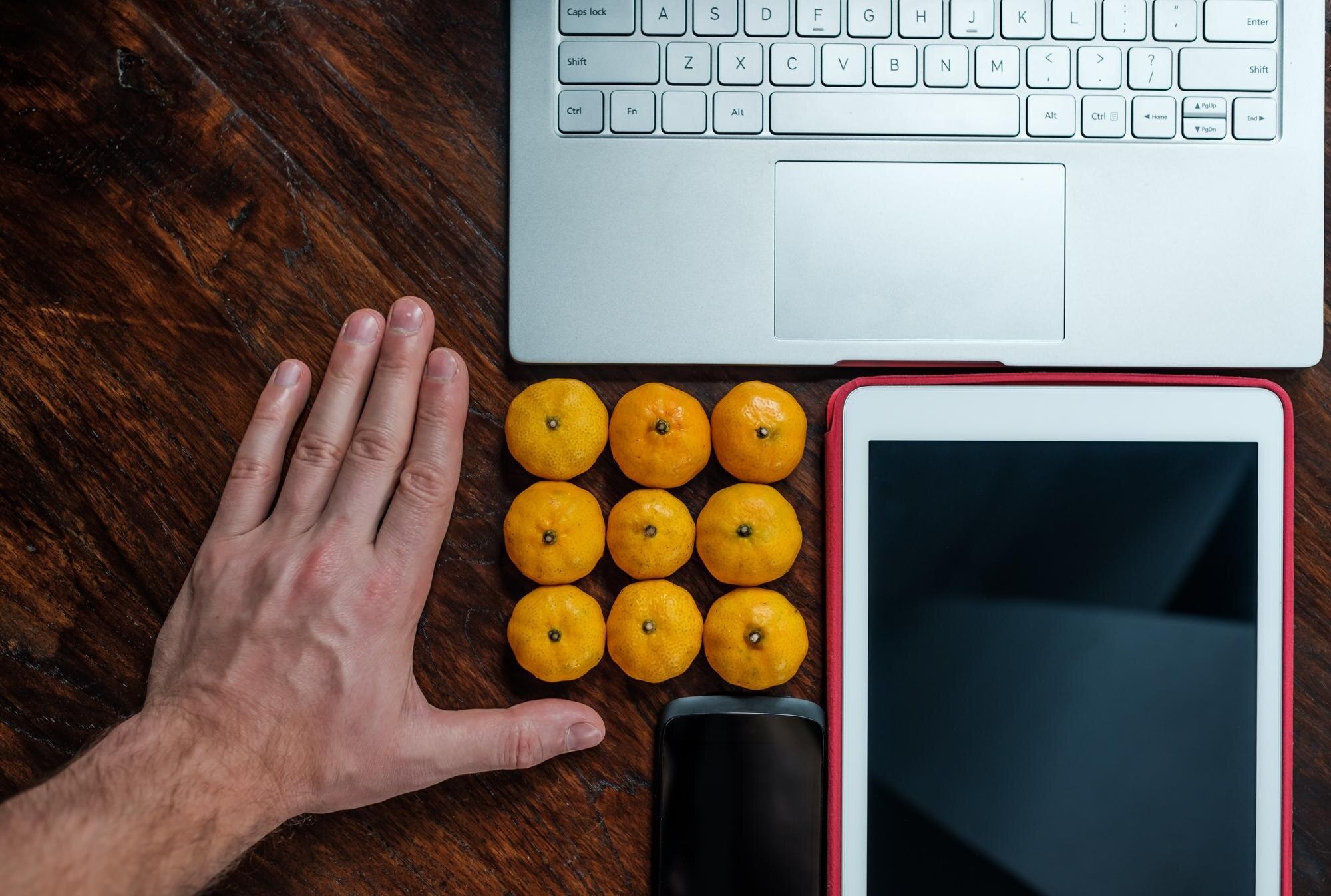 Mężczyzna położył mandarynki obok laptopa i tabletu