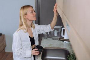 Młoda kobieta wyciąga kubek z kawą z szuflady w kuchni