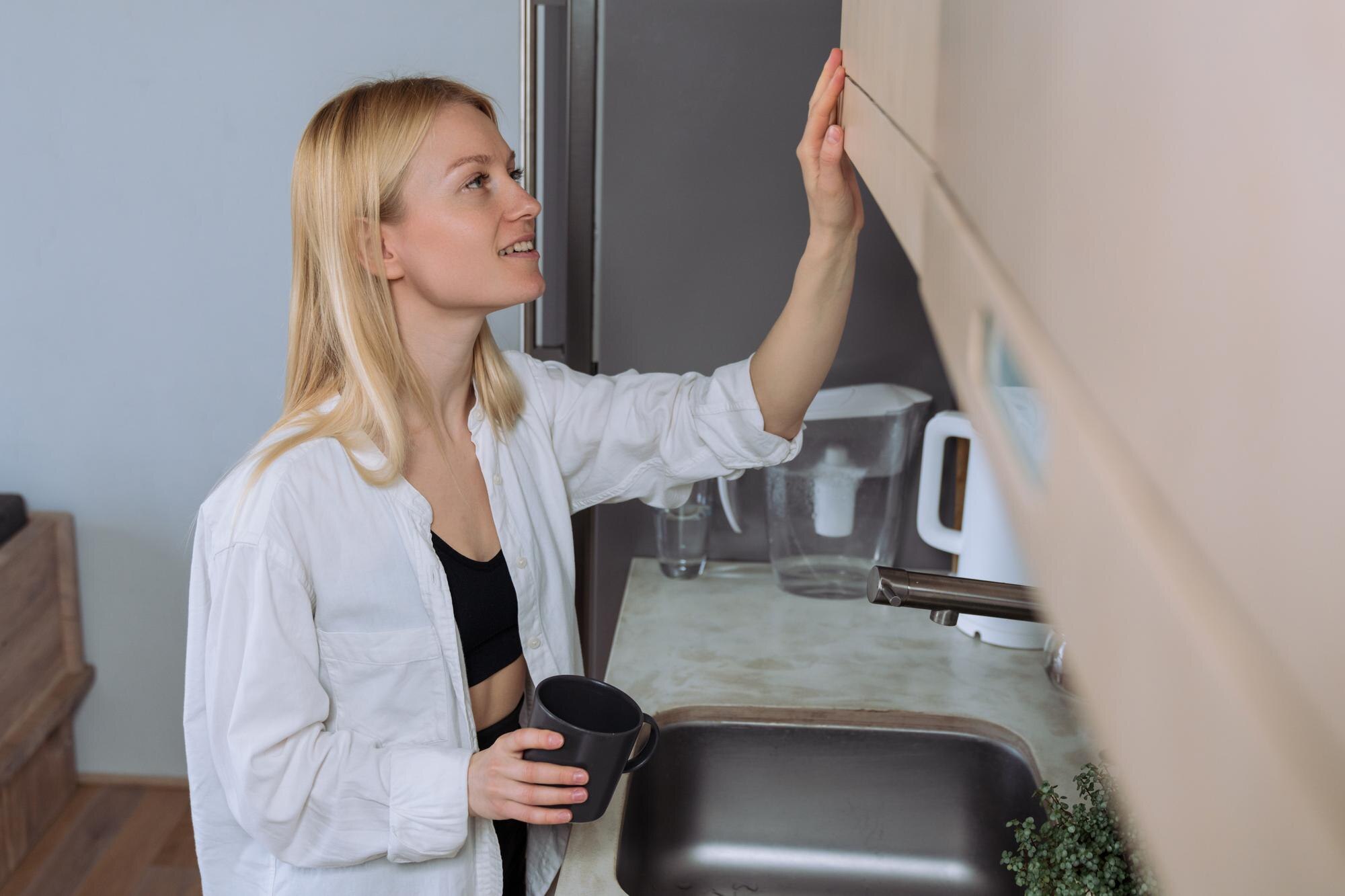 Młoda kobieta wyciąga kubek z kawą z szuflady w kuchni