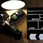 Klakier filmowy z kamerą, mikrofonem i taśmą VHS na drewnie.