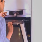 Piękna młoda kobieta sprawdza, jak radzi sobie jej ciasto w piekarniku