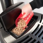 Zbliżenie na pelety czarny domowy piec na pelety człowiek ładujący ręcznie granulki z czerwonym kubkiem z nadrukiem 3 d