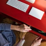 Kobieta otwiera szufladę biurka i chce wziąć stamtąd coś, na czym stoi komputer