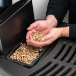 Piec na pellet mężczyzna trzymający granulat w dłoni nad nowoczesnym czarnym piecem