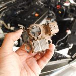 Stary prostownik samochodowy alternator trzymany przez mechanika samochodowego z rozmytym tłem komory silnika samochodu