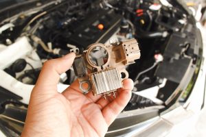 Stary prostownik samochodowy alternator trzymany przez mechanika samochodowego z rozmytym tłem komory silnika samochodu