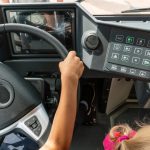 Zbliżenie dłoni dziecka na kierownicy autobusu Dziecko w kabinie samochodu Widok na kierownicę i deskę rozdzielczą nowego nowoczesnego autobusu Miejski transport publiczny