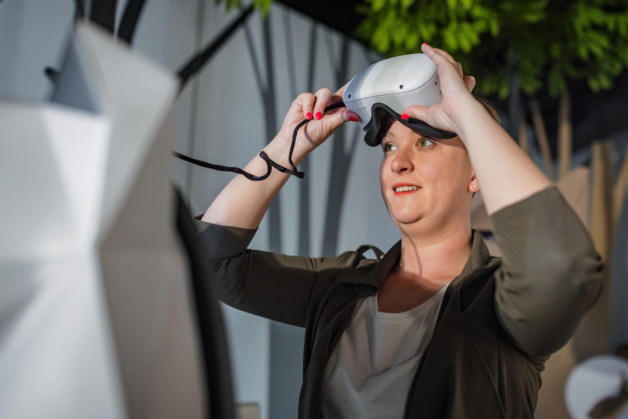 Uśmiechnięta kobieta bawiąca się z headsetem wirtualnej rzeczywistości w pokoju VR podczas historii naturalnej