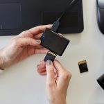 ręce z czytnikiem kart SD, laptopem i kamerą