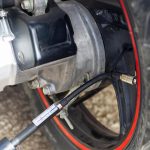 Koło motocykla z podłączoną sprężarką powietrza w celu napompowania ciśnienia w oponach