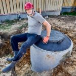Pracownik zmontował drugą komorę zbiornika septicznego z betonowych pierścieni i usiadł odpocząć na otworze