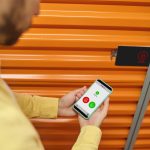 Przycięte zdjęcie rąk mężczyzny trzymającego telefon obok drzwi magazynu