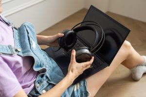 Duże czarne słuchawki w rękach siedzącej dziewczyny przy laptopie