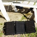 Bateria słoneczna leży na ziemi w pobliżu plastikowego krzesła, na którym ładowany jest telefon komórkowy Koncepcja alternatywnego źródła energii