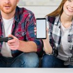 Uśmiechnięta dziewczyna siedzi z chłopakiem, gra wideo pokazuje ekran telefonu komórkowego