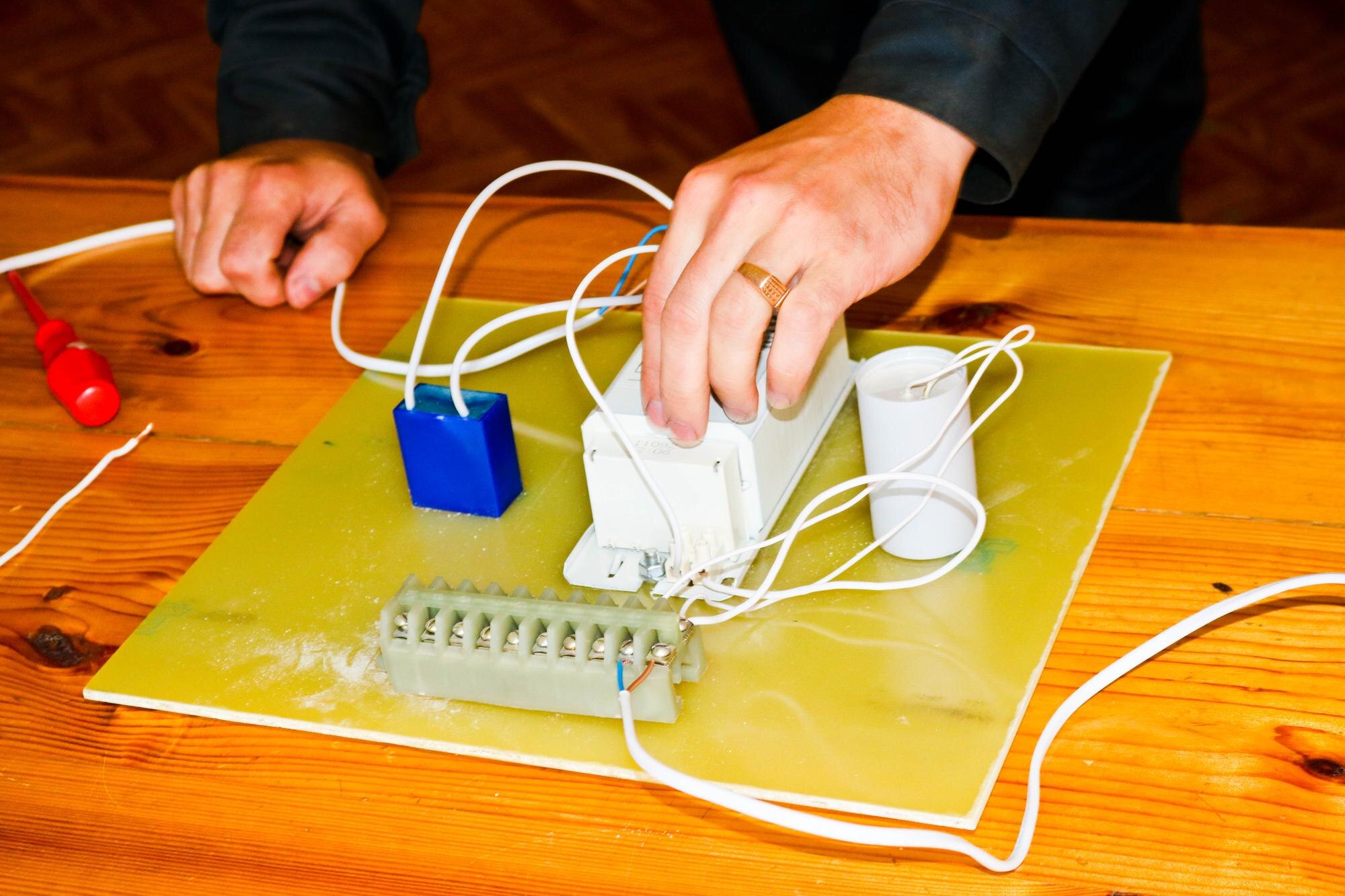 Mężczyzna pracujący jako elektryk zbiera obwód elektryczny dużej białej lampy ulicznej