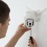 Technik z śrubokrętem instalujący kamerę CCTV na ścianie w pomieszczeniach