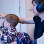 Chłopiec siedzi na ramionach nastolatka, a starszy brat pokazuje mu zdjęcie na monitorze.