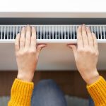 Kobieta ogrzewa ręce w pobliżu nowoczesnego grzejnika w pokoju w domu powyżej widoku zbliżonego