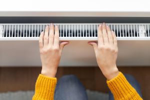 Kobieta ogrzewa ręce w pobliżu nowoczesnego grzejnika w pokoju w domu powyżej widoku zbliżonego