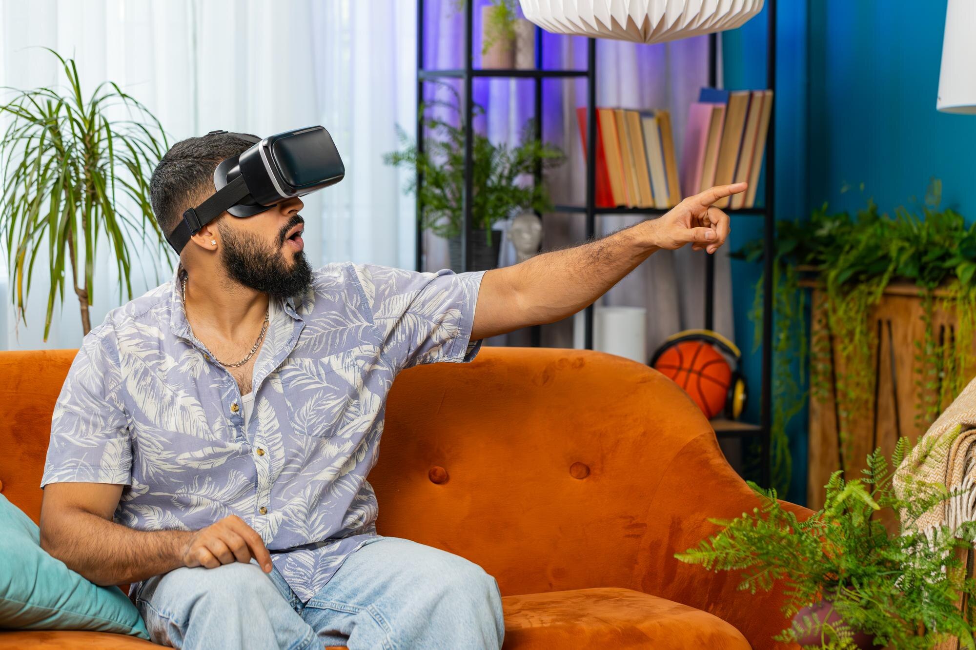 Indyjski mężczyzna używający wirtualnej rzeczywistości futurystycznej technologii słuchawki grać w symulację 3D gry wideo w domu