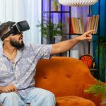 Indyjski mężczyzna używający wirtualnej rzeczywistości futurystycznej technologii słuchawki grać w symulację 3D gry wideo w domu