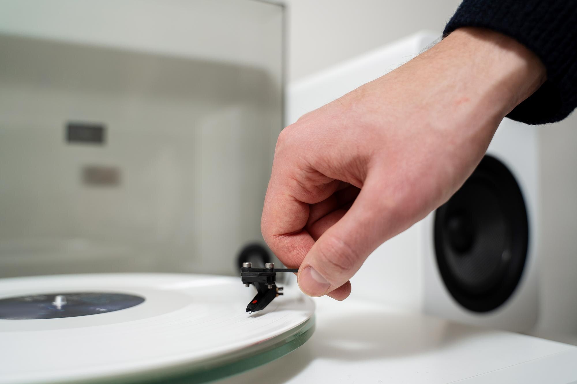Muzyk umieszcza białą płytę winylową na gramofonie, aby cieszyć się ścieżkami dźwiękowymi z HiFi i LP Biały odtwarzacz winylu z systemem głośników i płytą rockową w białym cieniu
