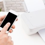 Użytkownik obsługuje smartfon podłączony do drukarki w nowoczesnym pomieszczeniu roboczym w ciągu dnia