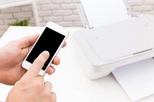 Użytkownik obsługuje smartfon podłączony do drukarki w nowoczesnym pomieszczeniu roboczym w ciągu dnia