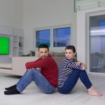 Wesoła młoda para siedzi plecami do siebie na podłodze w domu