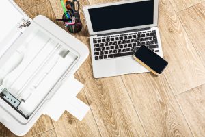 Nowoczesna przestrzeń robocza wyposażona w laptop, smartfon i drukarkę na drewnianej podłodze w jasnym otoczeniu biurowym