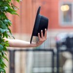 Ręka trzymająca czarny kapelusz w pobliżu zielonej ściany rośliny w środowisku miejskim