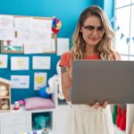 Młoda blondynka nauczycielka za pomocą laptopa stojącego w przedszkolu