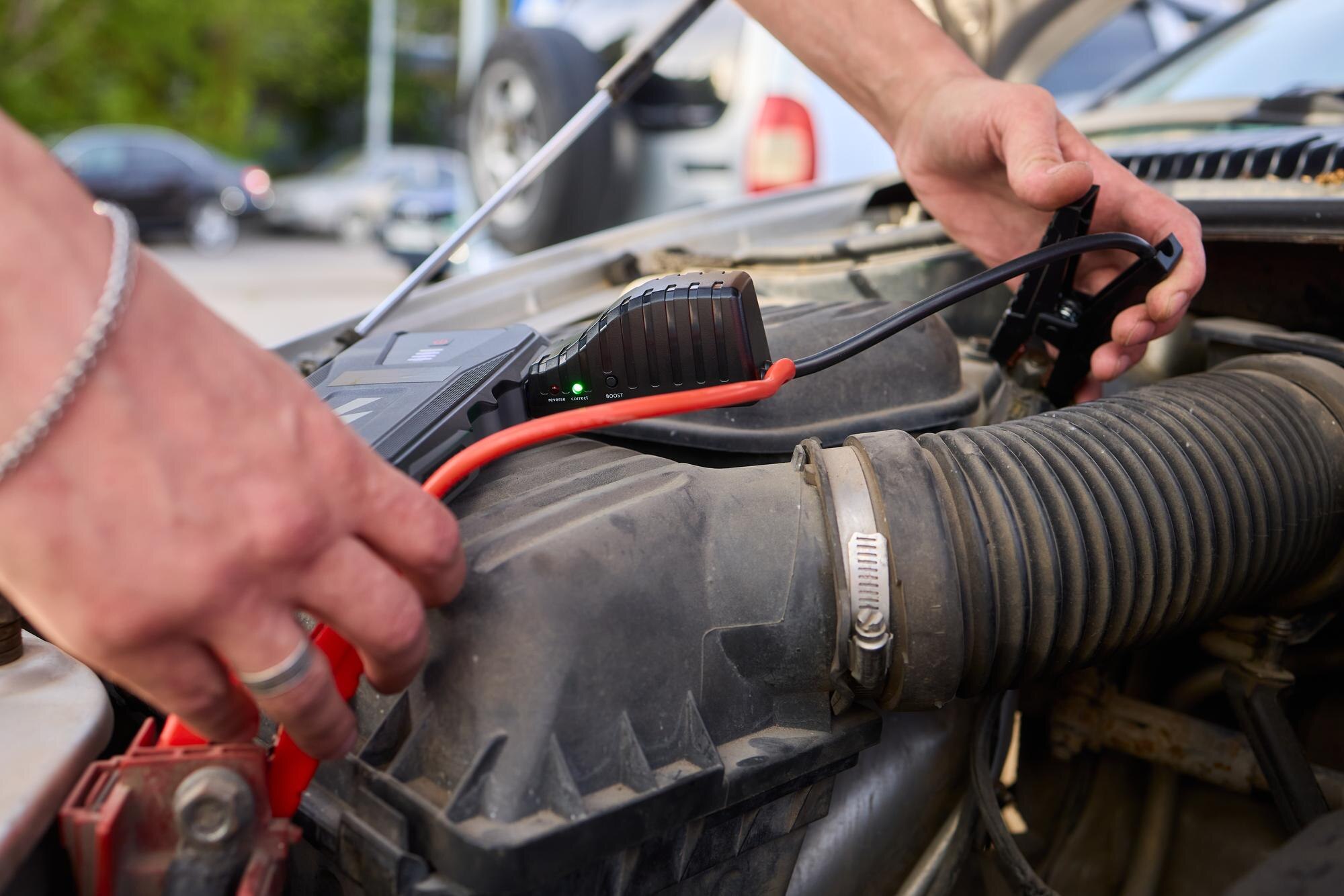 Zbliżone zdjęcie czarnego akumulatora samochodowego podłączonego do kabli jumperów do naprawy lub ładowania