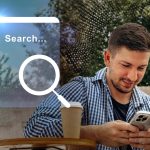 Man using smartphone to search online while enjoying coffee outdoors in urban setting during daytime