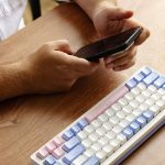 Osoba korzystająca ze smartfona z kolorową klawiaturą na drewnianym stole w godzinach porannych