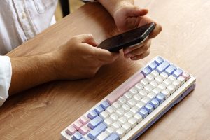 Osoba korzystająca ze smartfona z kolorową klawiaturą na drewnianym stole w godzinach porannych