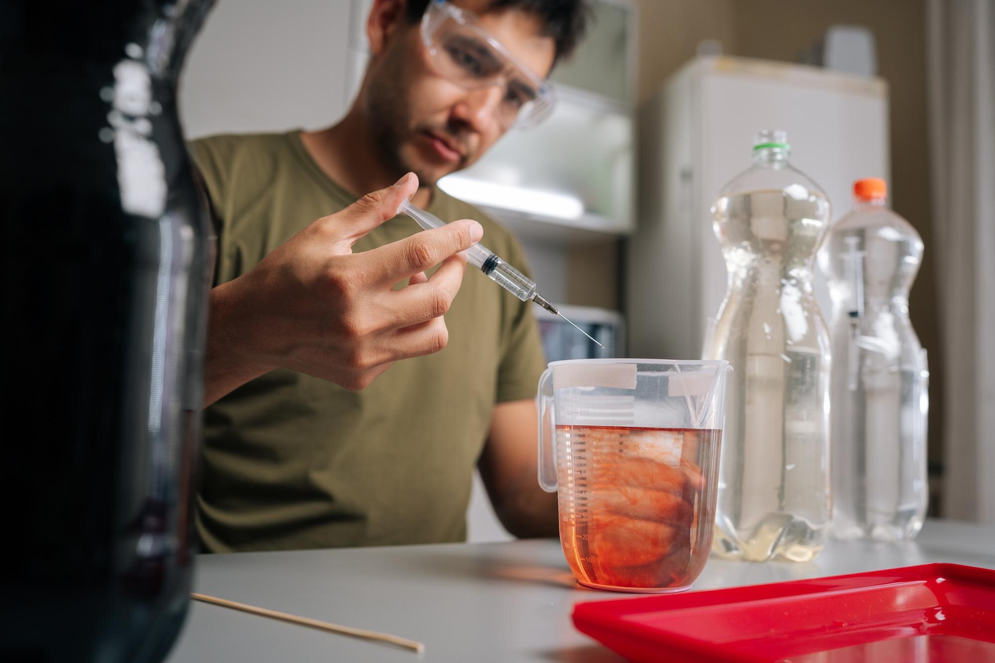 Home gardening enthusiast in safety glasses adding red liquid fertilizer to water in beaker using