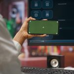 Woman using green screen smartphone to learn how to use ai llm chatbot on computer screen in home